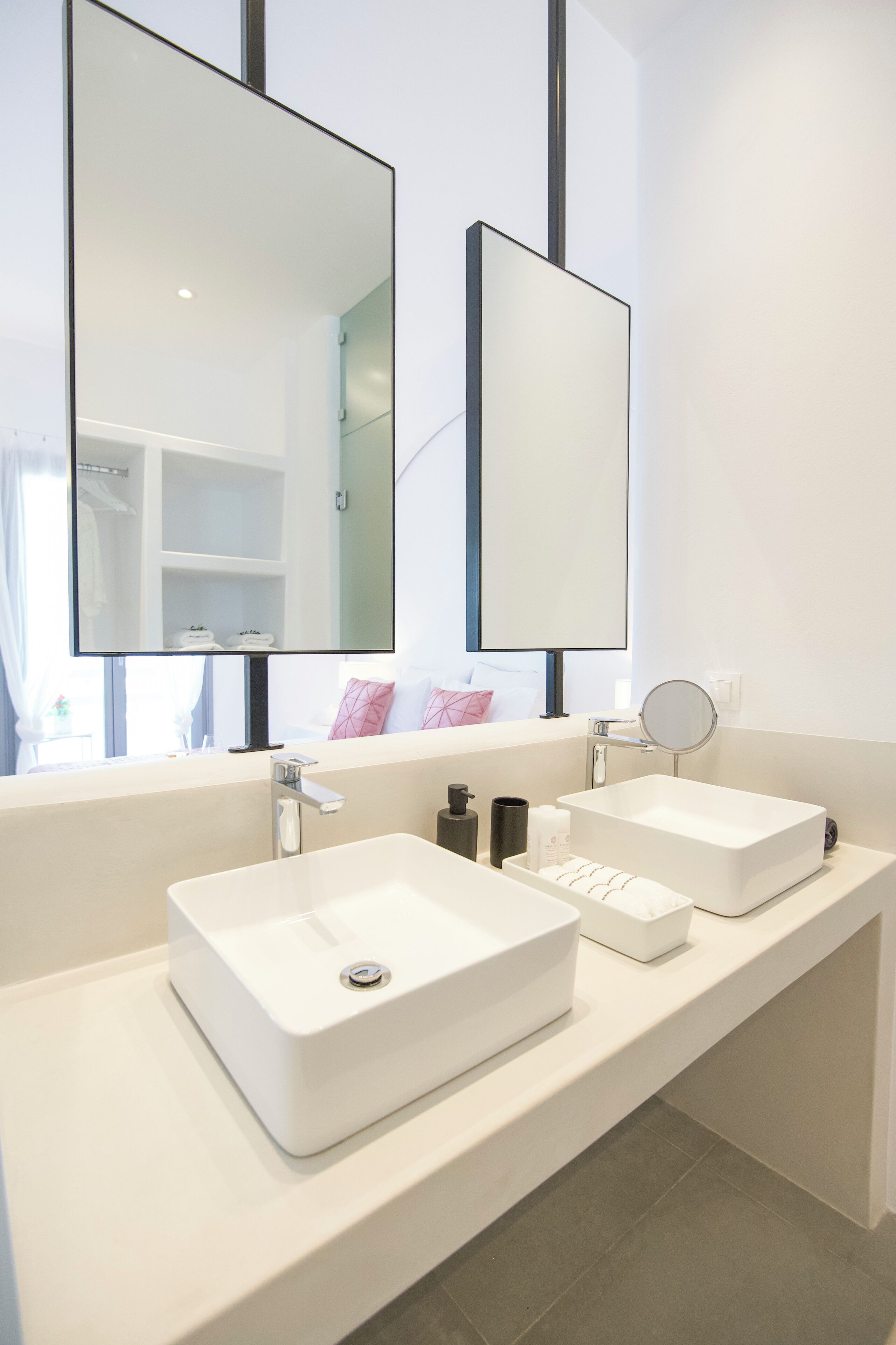 A modern bathroom with two white sinks, a large mirror, and a small round mirror.