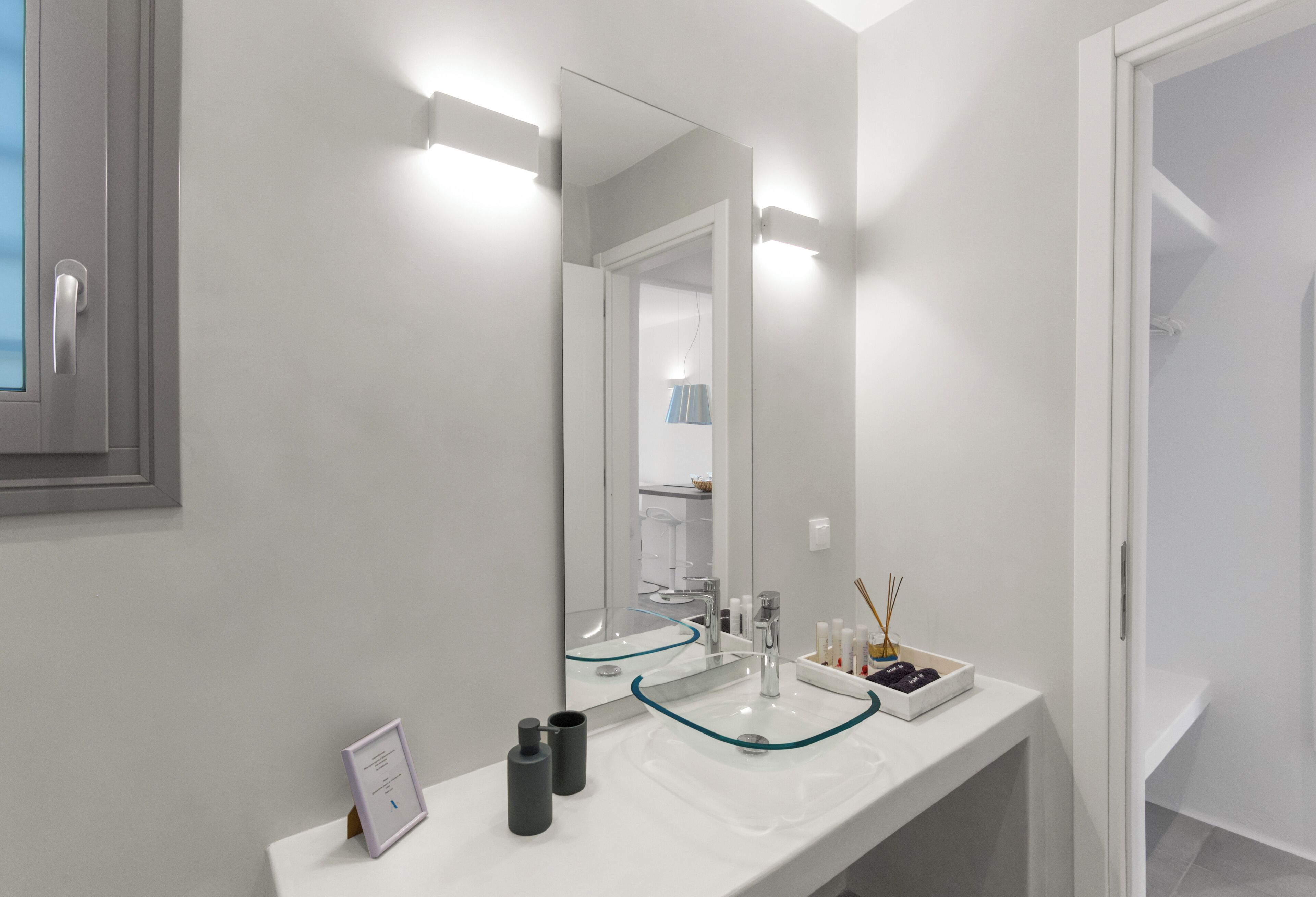 A modern bathroom with a white sink, a large mirror, and a glass-fronted cabinet.