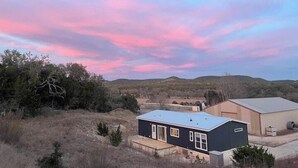 A modern two-story house with a flat roof, large windows, and a covered patio area. - Cedar Ranch House Rental (Bandera)