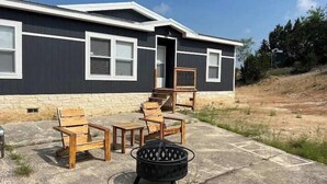 A house with a stone foundation, a patio with wooden furniture, and a black fire pit. - Cedar Ranch House Rental (Bandera)