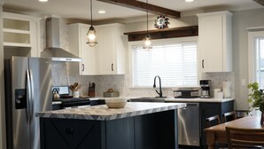 A modern kitchen with a large island, stainless steel appliances, and pendant lighting. - Cedar Ranch House Rental (Bandera)