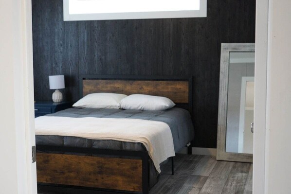 A bedroom with a dark wooden headboard, a bed with white and gray bedding, and a nightstand with a lamp.
