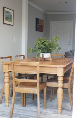A wooden dining table with six chairs, a potted plant, and framed artwork on the wall.