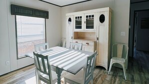 Un coin repas comprenant une table et des chaises, une fenêtre avec des stores et un meuble blanc aux portes vitrées.