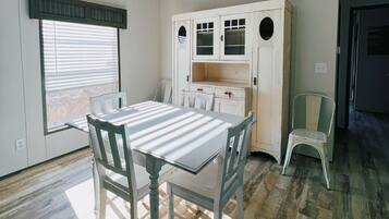 A dining area with a table and chairs, a window with blinds, and a white cabinet with glass doors.
