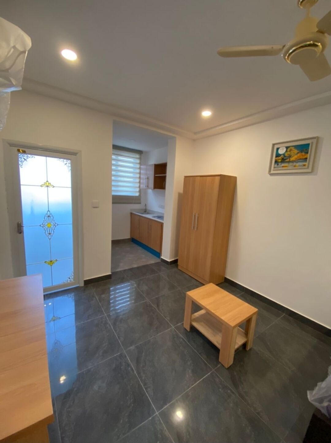 A room with a tiled floor, a wooden table, a wardrobe, a ceiling fan, and a door with a stained glass design.