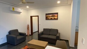 Un salon moderne avec deux canapés, une table basse et une table à manger. On y trouve un ventilateur de plafond, un appareil de climatisation et un tableau encadré au mur.