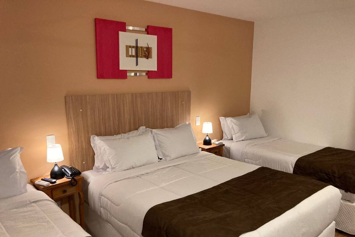 Une chambre d’hôtel avec deux lits, une tête de lit en bois, des lampes de chevet et une œuvre d’art accrochée au mur.