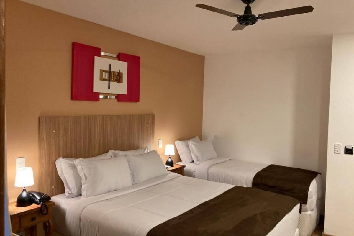 Une chambre d’hôtel avec deux lits, un ventilateur de plafond, une œuvre d’art accrochée au mur, des lampes de chevet et un téléphone.