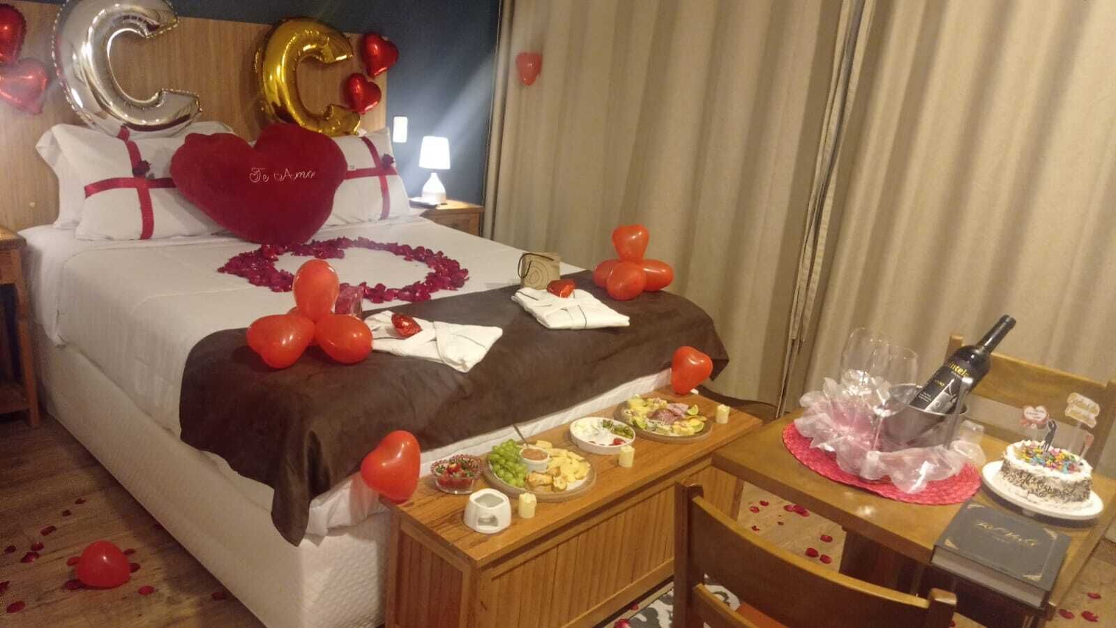 A hotel room with a bed, a bedside table with food and drinks, and a chair.