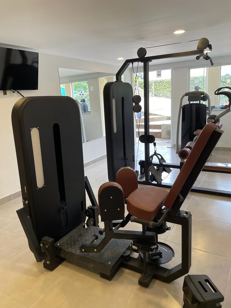 Uma academia com equipamentos de exercício, uma televisão fixada na parede e amplas janelas.