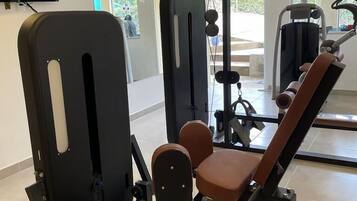 Uma academia com equipamentos de exercício, uma televisão fixada na parede e amplas janelas.