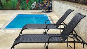 Zona de piscina con un mural de un leopardo, dos sillas reclinables negras y una pequeña mesa redonda.