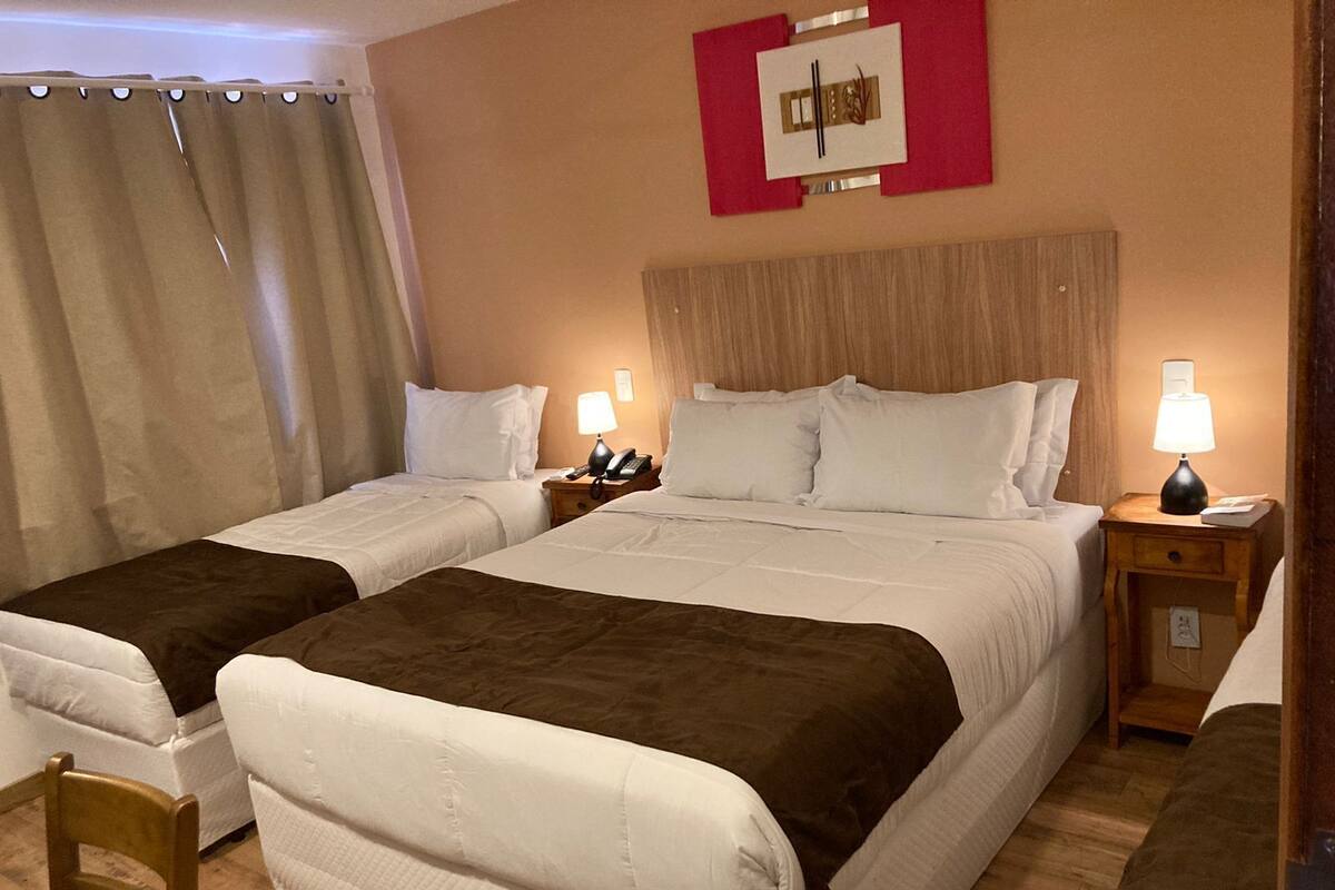 Une chambre d’hôtel avec deux lits, une tête de lit en bois, des lampes de chevet, un téléphone et une œuvre d’art accrochée au mur.