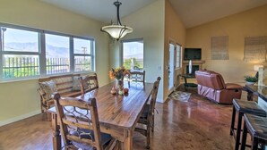 A dining area with a wooden table and chairs, a hanging light fixture, and a view of the outdoors through large windows.