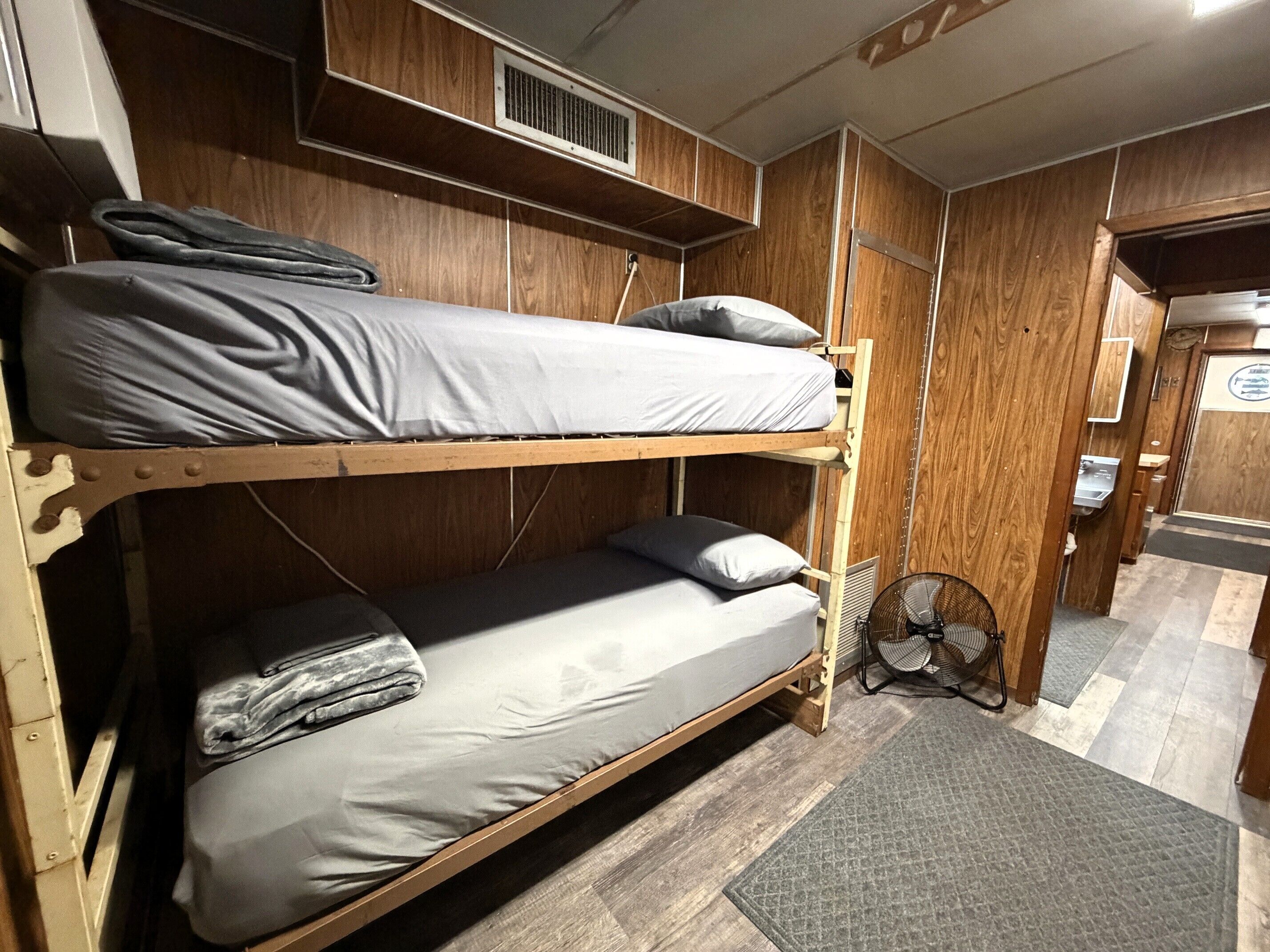 A bunk bed with a fan and a sink in a wooden cabin-style room.
