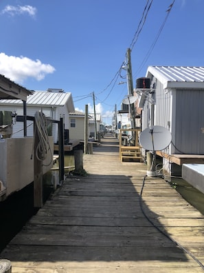 A narrow wooden walkway between mobile homes with satellite dishes and utility poles.