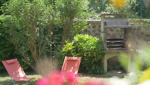 Un jardin avec un espace barbecue et deux chaises rouges.