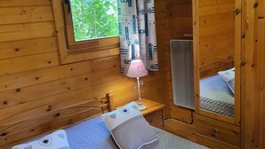 Une chambre dans un chalet en bois, avec un lit, deux oreillers, une table de chevet, une lampe et une fenêtre avec des rideaux.
