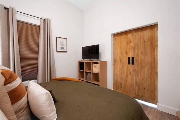 A bedroom with a bed, a television on a wooden stand, a wardrobe, and a window with curtains. - This townhouse is a 1 bedroom(s), 1 bathrooms, located in Wichita, KS. (Wichita)