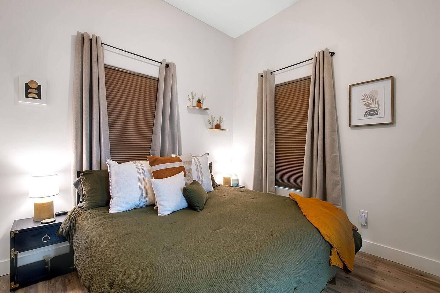 Une chambre à coucher comprenant un lit, des oreillers, une table de chevet, une lampe, une étagère murale agrémentée d’objets décoratifs et un tableau encadré accroché au mur.