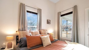 A bedroom with a large bed, two bedside tables, a window with curtains, and a view of the outside. - This townhouse is a 1 bedroom(s), 1 bathrooms, located in Wichita, KS. (Wichita)