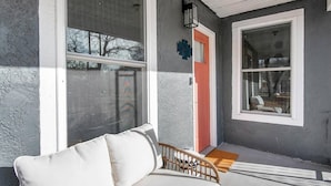 A covered porch with a white chair, a red door, and a window with a view of the outside. - This townhouse is a 1 bedroom(s), 1 bathrooms, located in Wichita, KS. (Wichita)