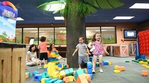 Des enfants jouent avec des blocs de construction colorés dans une pièce où se trouve un arbre et une pancarte indiquant « Ours et amis ».