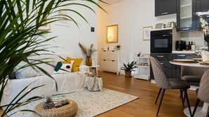 Una sala moderna con un sofá, una mesa de centro y un comedor con sillas, y una cocina al fondo.