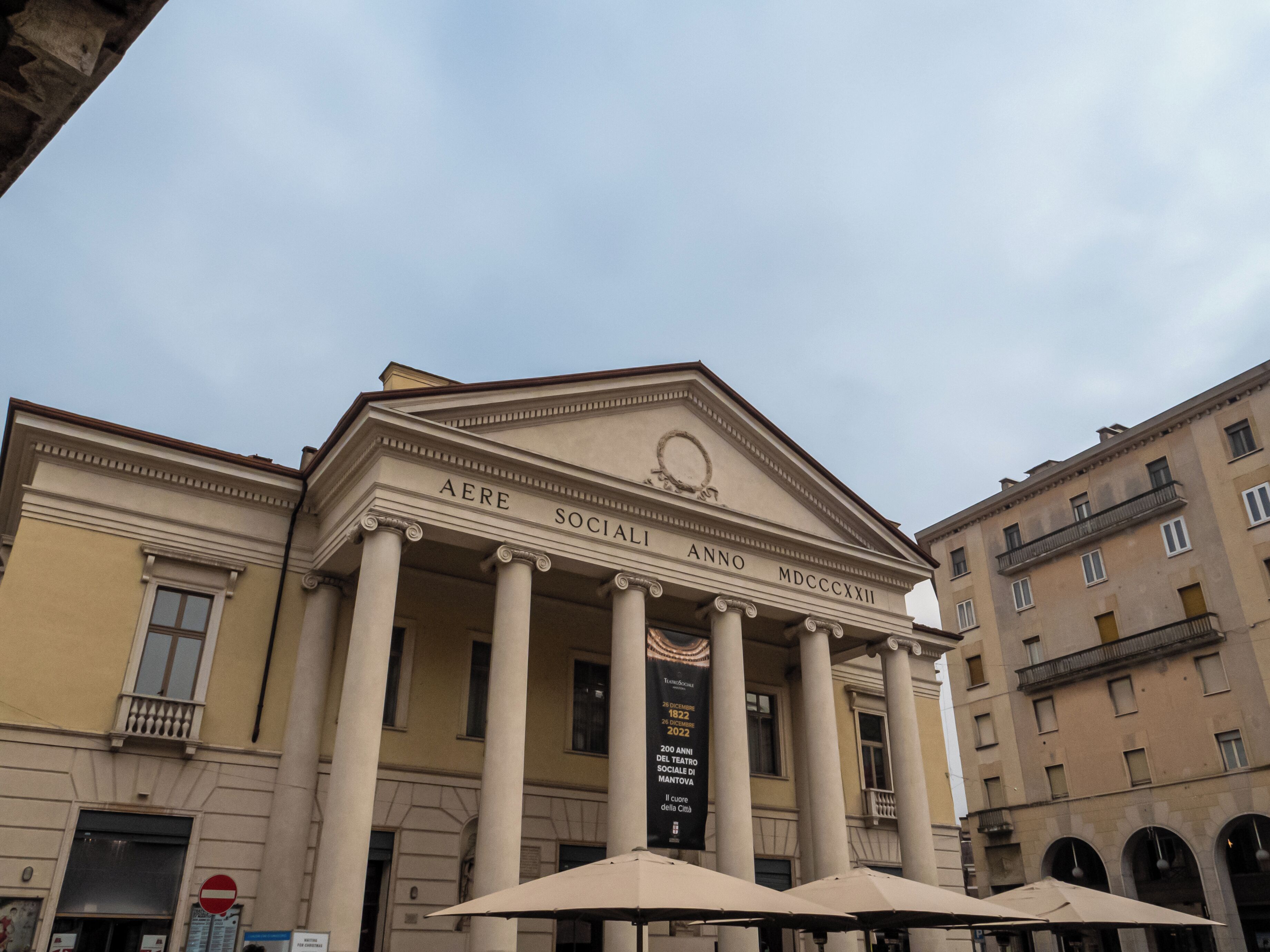 Un edificio neoclassico con colonne, un timpano e uno striscione che indica un anniversario di un teatro sociale.