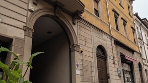 Un edificio con una gran entrada arqueada, una puerta con un letrero y un pequeño toldo.