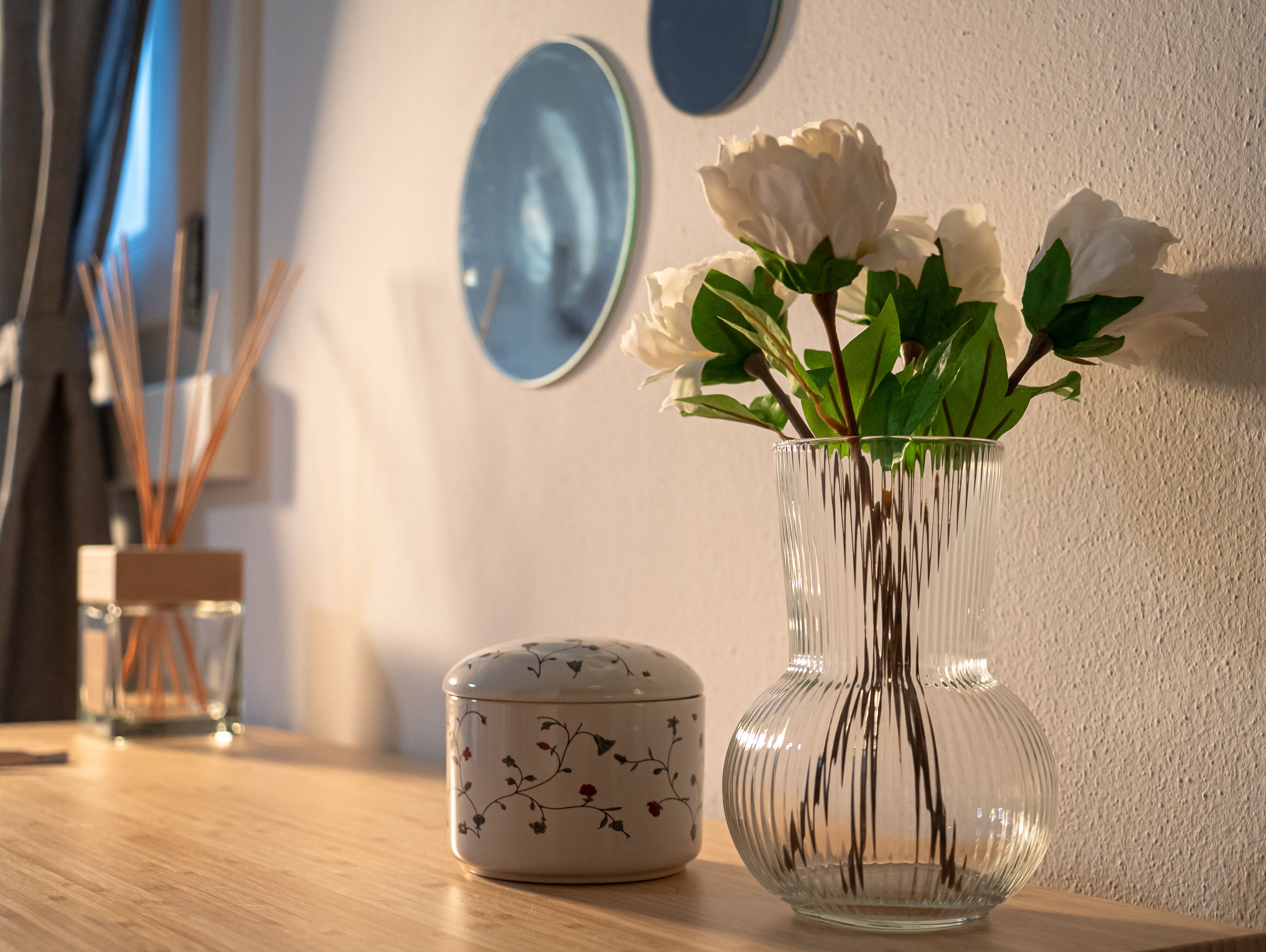Un vase en verre transparent contenant des fleurs blanches, posé sur une table en bois.