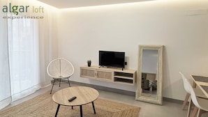 Una sala de estar moderna con una mesa redonda, una silla blanca, un televisor sobre un mueble de madera y un espejo grande.