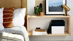Un dormitorio ordenado con cabecera de madera, una mesita de noche con una planta, un cuadro enmarcado y una lámpara.