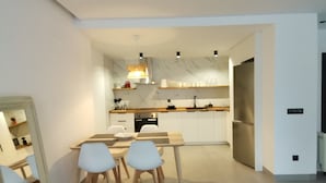 Una cocina moderna con armarios blancos, un refrigerador de acero inoxidable y un comedor con mesa y sillas.
