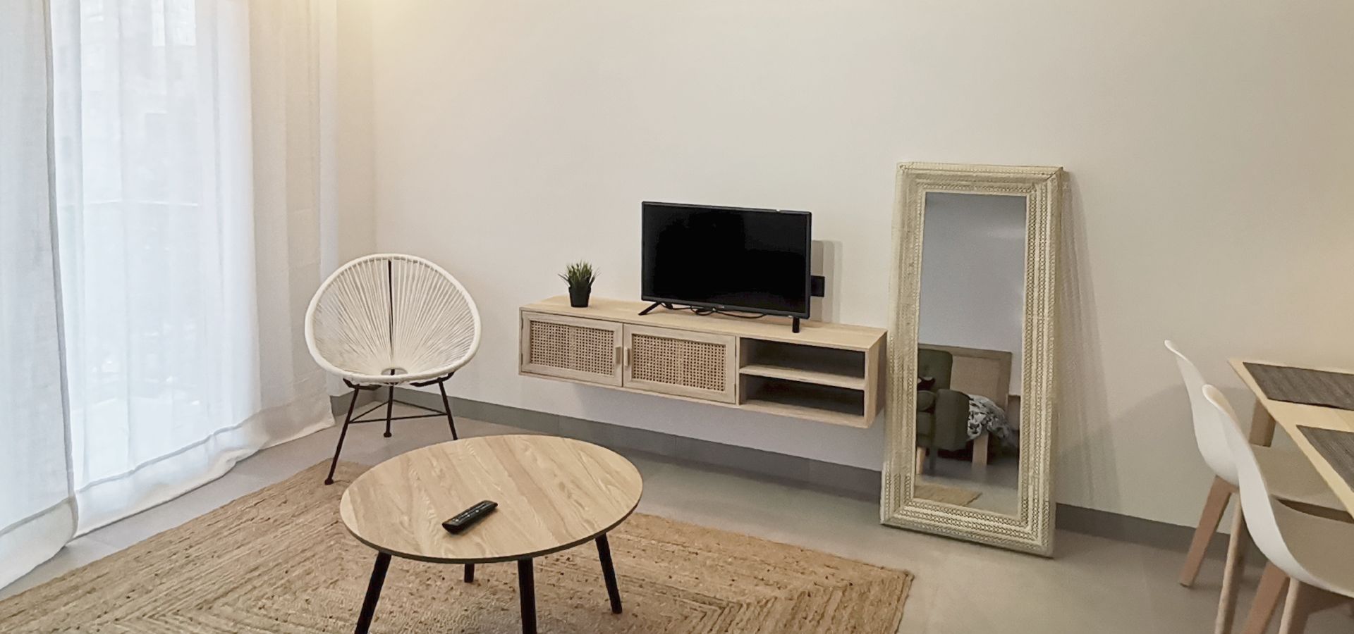 Ein modernes Wohnzimmer mit einem runden Tisch, einem weißen Sessel, einem Fernseher auf einem Holzboden und einem großen Spiegel.
