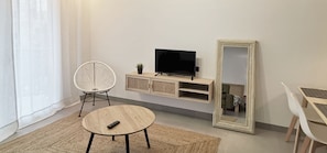 Ein modernes Wohnzimmer mit einem runden Tisch, einem weißen Sessel, einem Fernseher auf einem Holzboden und einem großen Spiegel.