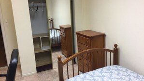 Een slaapkamer met een bed, een houten dressoir en een inloopkast met spiegel.