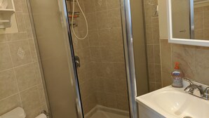 Een badkamer met een douchecabine van glas, een witte wastafel en een toilet.