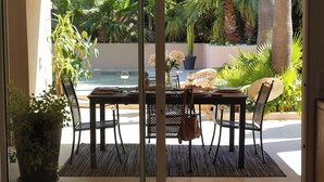 Un espace extérieur aménagé pour prendre les repas, avec une table dressée pour deux personnes, entourée de chaises, et offrant une vue sur des plantes tropicales et un palmier.
