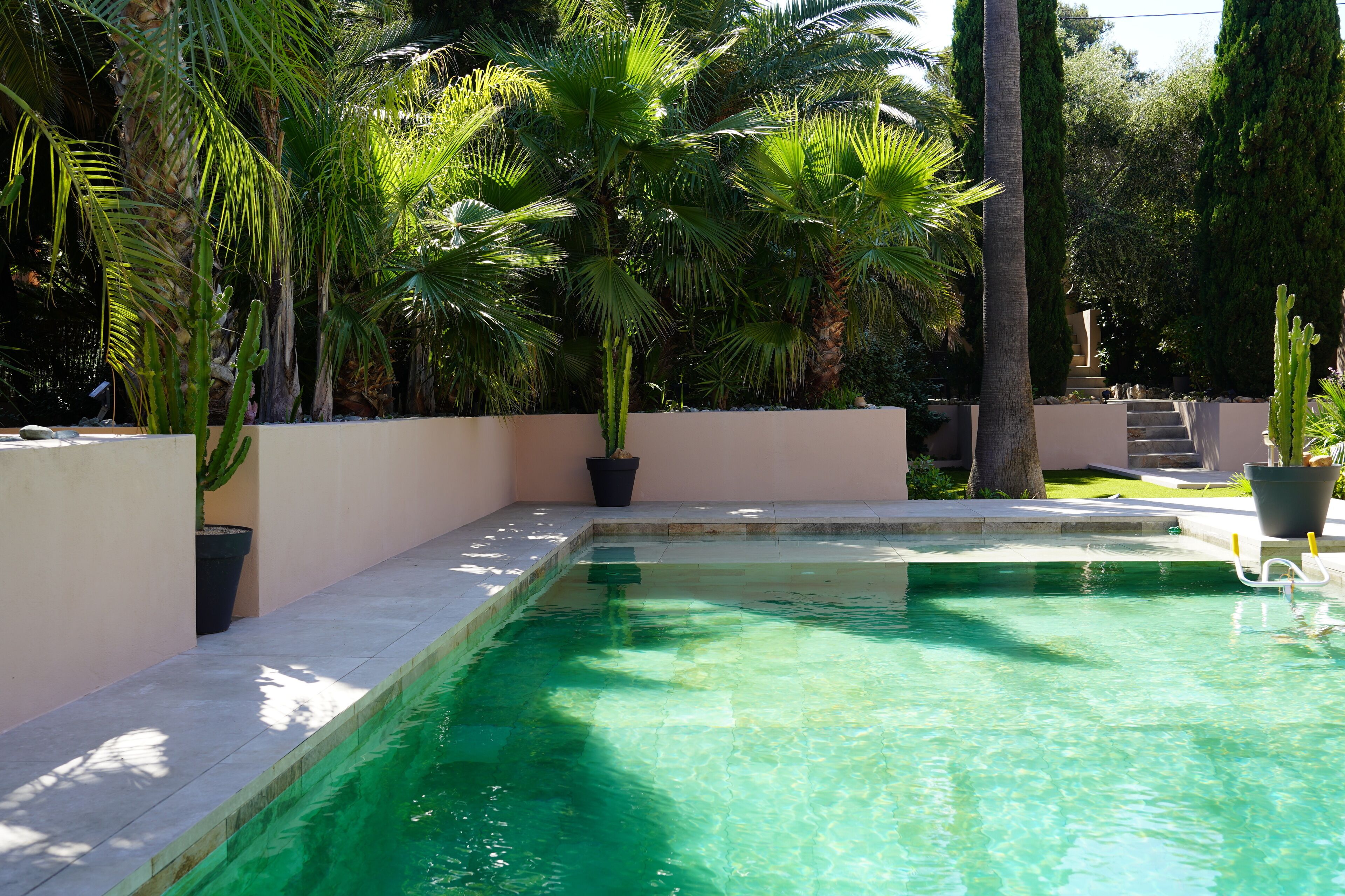 A rectangular swimming pool with clear water, surrounded by a low wall and potted plants.