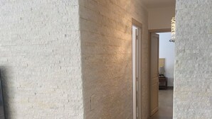 Un couloir avec un mur à texture et un plancher en bois, qui mène à une pièce dotée d’une porte.