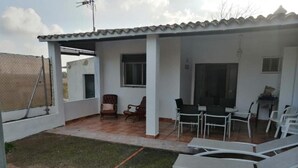 Ein überdachter Patio-Bereich mit Gartenmöbeln, darunter Stühle und Tische, und einer kleinen Rasenfläche.