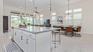 A spacious kitchen with a large island, modern pendant lights, and a dining area with a TV and artwork. - Cave Creek Gem! New Construction! (Cave Creek)