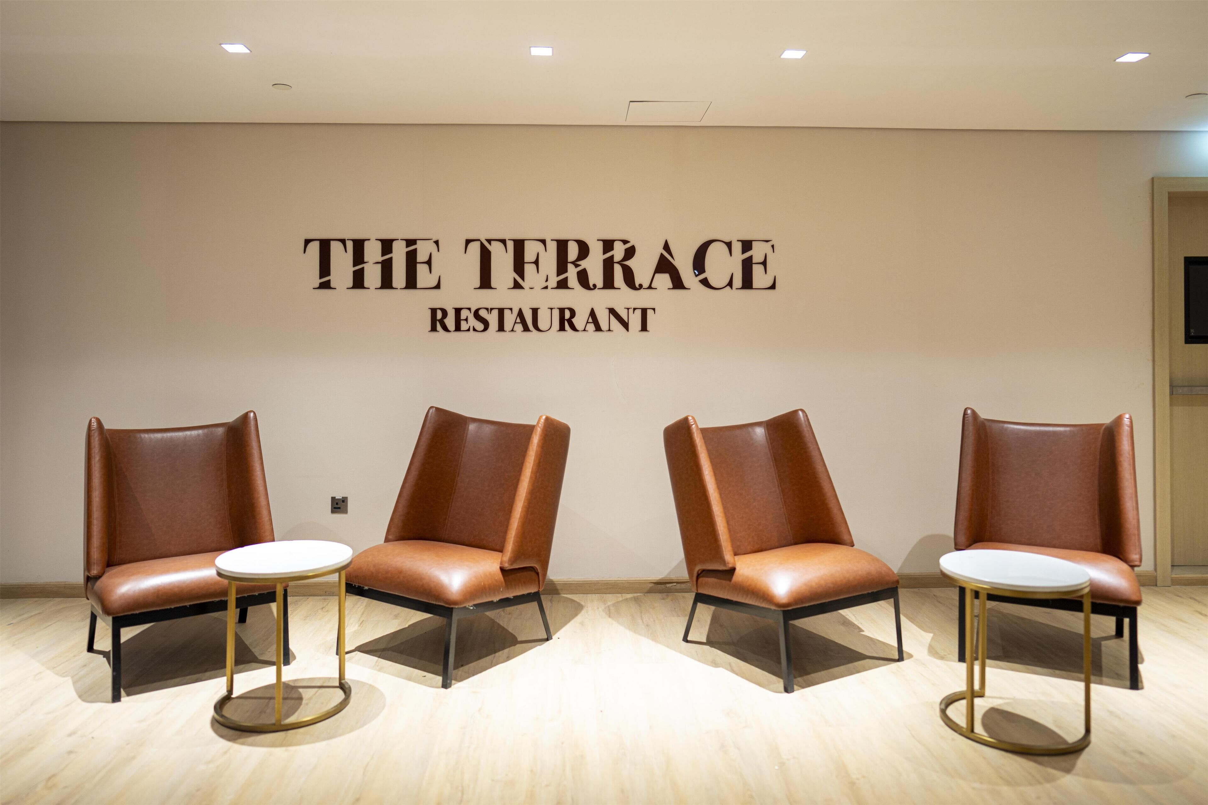 A restaurant interior with a modern design, featuring leather chairs and small round tables.