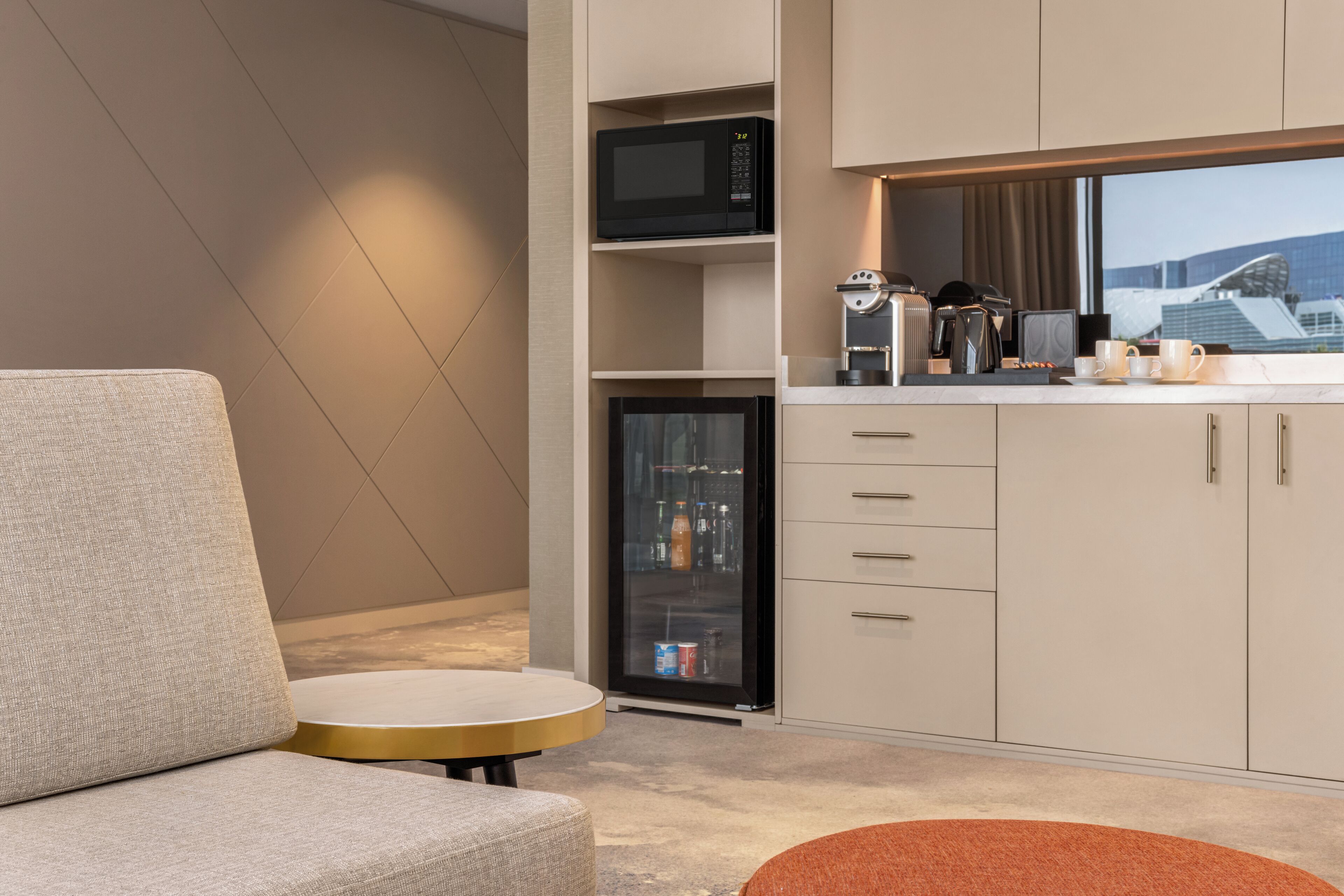 Une kitchenette moderne équipée d’un four à micro-ondes, d’un réfrigérateur et d’une machine à café. Le salon comprend une table ronde et un canapé.