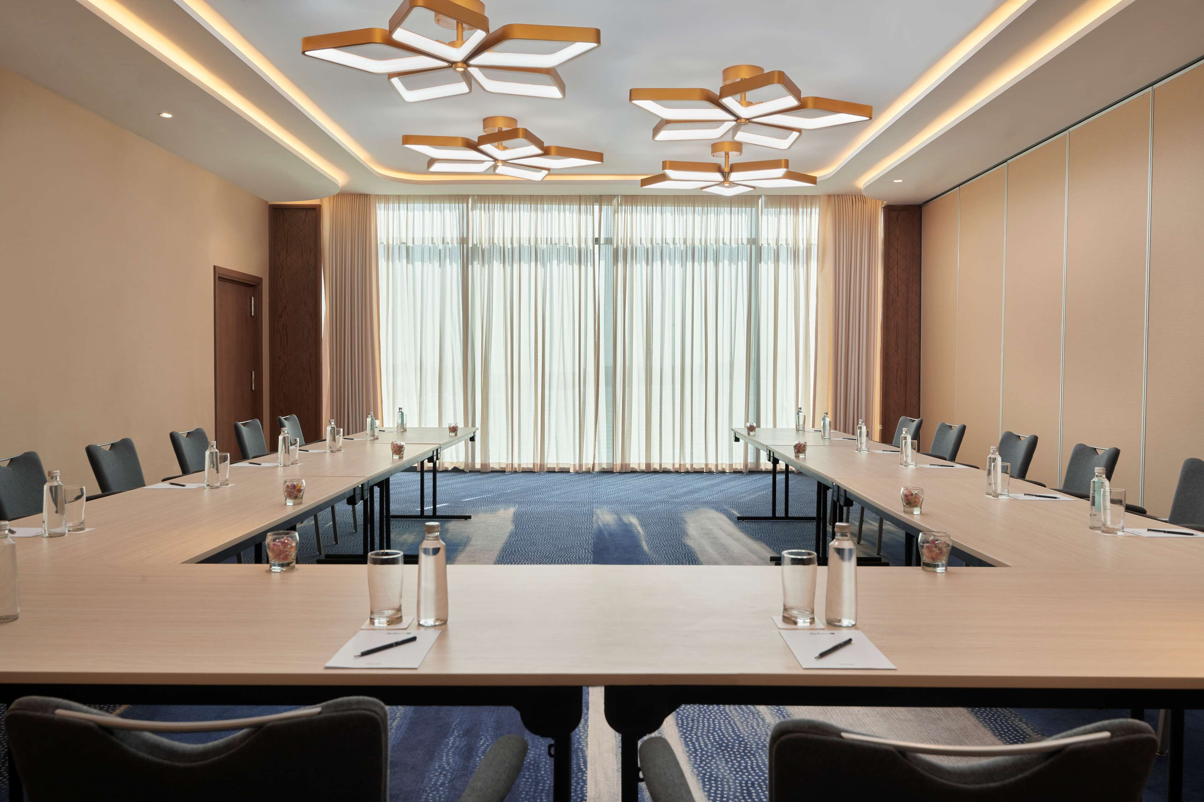 Un salón de conferencias con una larga mesa, sillas e iluminación moderna en el techo.