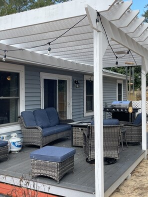 A covered patio with wicker furniture, a grill, and string lights. - Family cottage by boat launch, minutes to Navarre or Pensacola Beach! (Gulf Breeze)