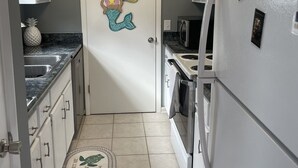 A narrow kitchen with white cabinets, a white refrigerator, a stove, and a microwave. There is a decorative mermaid on the door and a pineapple on the counter. - Family cottage by boat launch, minutes to Navarre or Pensacola Beach! (Gulf Breeze)