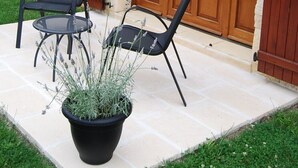 Une terrasse avec deux chaises et un pot de fleurs devant un bâtiment en pierre, doté d’une porte en bois et de volets.